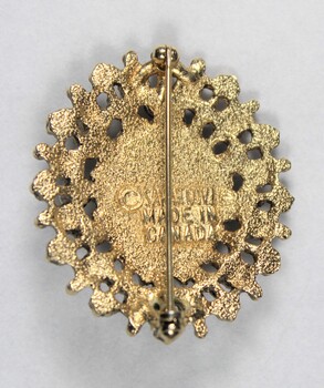 Back of an oval brooch from the Sarah Coventry jewellery range, with a pin clasp to attach it and a makers mark below the pin. 