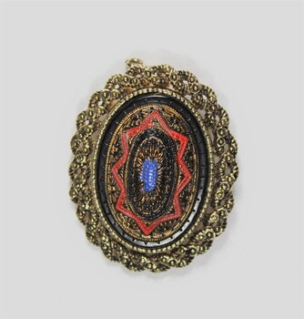 Front of an oval brooch in gold toned metal with red, blue and black inlay.