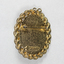 Back of an oval brooch in gold toned metal with red, blue and black inlay.