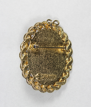 Back of an oval brooch in gold toned metal with red, blue and black inlay.