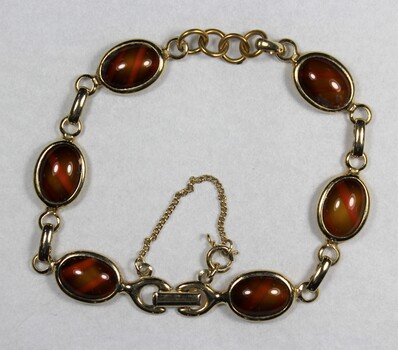 Front surface of a gold toned metal bracelet from the Sarah Coventry Pty. Ltd. jewellery range with small brown oval faux stones.