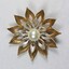 Front surface of a gold and silver toned metal brooch with a central faux pearl from the Sarah Coventry Pty. Ltd. jewellery range.