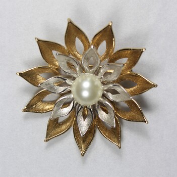 Front surface of a gold and silver toned metal brooch with a central faux pearl from the Sarah Coventry Pty. Ltd. jewellery range.