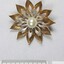 Front surface of a gold and silver toned metal brooch with a central faux pearl from the Sarah Coventry Pty. Ltd. jewellery range, with a 5 cm black and white scale.