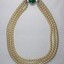 Front of a necklace with three strands of faux pearls and a faux green stone.