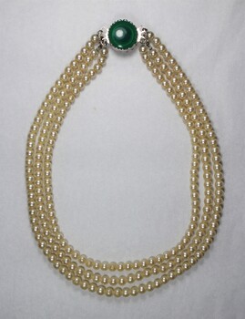 Front of a necklace with three strands of faux pearls and a faux green stone.