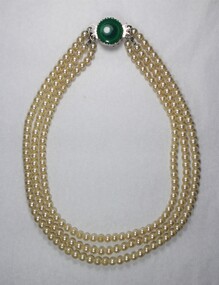 Front of a necklace with three strands of faux pearls and a faux green stone.
