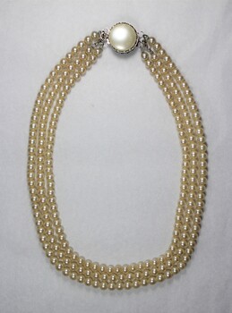 Back of a necklace  with three strands of faux pearls and a large faux pearl at the clasp.