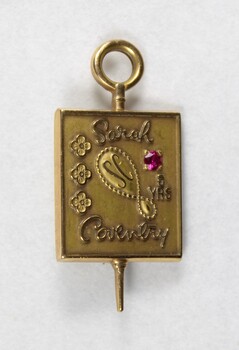 Front of a Sarah Coventry gold metal pin for five years service, with a faceted pink stone inlay on the proper left side.
