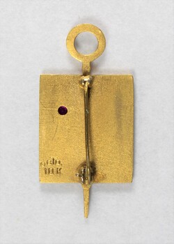 Back of a Sarah Coventry gold metal pin for five years service, with the back of a pink stone inlay and a makers stamp on the proper left side.