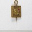 Front of a Sarah Coventry gold metal pin for five years service, with a faceted pink stone inlay on the proper left side and a 5 cm black and white scale.