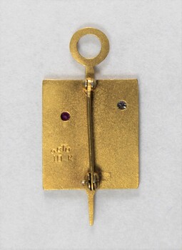 Back of a Sarah Coventry gold metal pin for ten years service, with a pink stone inlay on the proper left side and a clear stone on the proper right side.