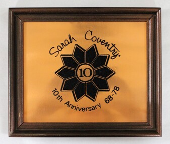Front of a brown wooden fame on a copper plaque commemorating Sarah Coventry 10th Anniversary from 68-78.