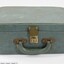Front of a green suitcase with a handle and a metal lock for a Sarah Coventry jewellery demonstration kit and a 5 cm black and white scale.