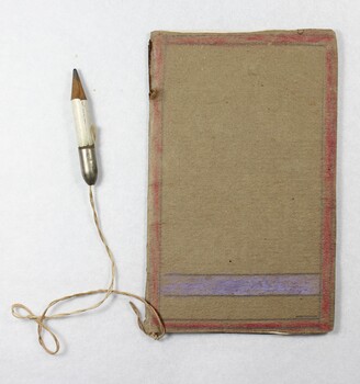 A handmade child's notebook with small white pencil attached by a piece of string. A hand drawn purple flower is on the front cover of the notebook, and the pages are blank.  