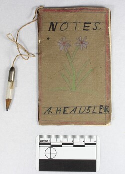 A handmade child's notebook with small white pencil attached by a piece of string. A hand drawn purple flower is on the front cover of the notebook, and the pages are blank.  