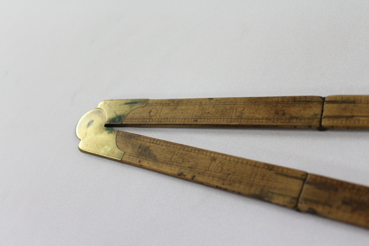Wooden fold out carpenter ruler with bendable brass hinges and imperial measurements engraved into the wood, detail of brass hinge.