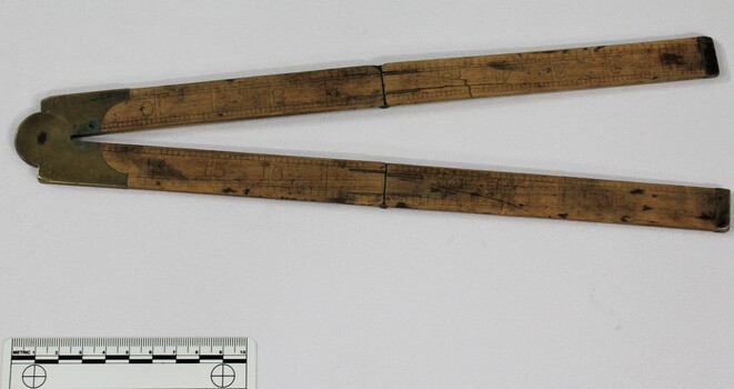 Wooden fold out carpenter ruler with bendable brass hinges and imperial measurements engraved into the wood, pictured with 10cm scale