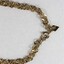 Detail of a gold toned metal chain with a rhombus-shaped attachment next to the clasp, with the Sarah Coventry mark stamped on it.
