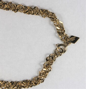 Detail of a gold toned metal chain with a rhombus-shaped attachment next to the clasp, with the Sarah Coventry mark stamped on it.