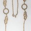 Gold toned metal chain with two circular elements and two swirling elements.