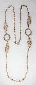 Gold toned metal chain with two circular elements and two swirling elements.