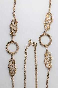 Detail of the two circular elements and two swirling decorative elements, as well as the clasp and small rhombus-shaped attachment near the clasp.