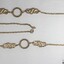 Gold toned metal chain with two circular elements and two swirling elements, with a black and white 5 cm scale.
