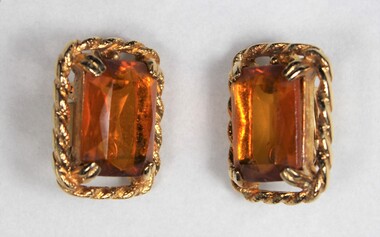 The front of two gold toned metal clip-on earrings with rectangular brown glass settings.