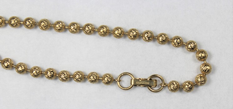 Detail of a gold toned beaded metal chain from the Sarah Coventry jewellery range, showing the clasp with the Sarah Coventry mark stamped on it.
