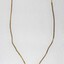 Front of a gold toned metal neckalce with an oval-shaped pendant inlaid with a brown resinous material.