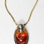 Detail of the front of a gold toned metal neckalce with an oval-shaped pendant inlaid with a brown resinous material.