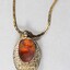 Detail of the back of the gold toned metal necklace with an oval-shaped pendant inlaid with a brown resinous material.