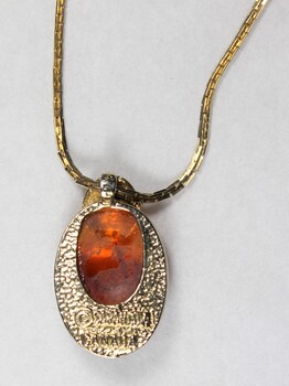 Detail of the back of the gold toned metal necklace with an oval-shaped pendant inlaid with a brown resinous material.
