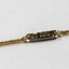 Detail of the back of the clasp on the gold toned metal chain with the oval-shaped pendant with the patent number.