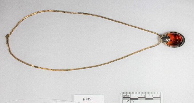 Front of a gold toned metal necklace with an oval-shaped pendant from the Sarah Coventry jewellery range with a black and white 5 cm scale.