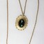Front of a gold toned metal cable chain necklace with an oval pendant and a faceted green/brown glass setting.