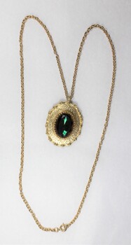 Front of a gold toned metal cable chain necklace with an oval pendant and a faceted green/brown glass setting.