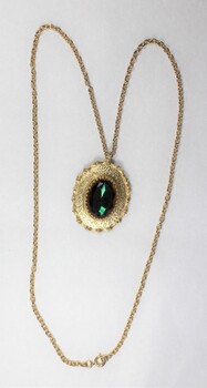 Front of a gold toned metal cable chain necklace with an oval pendant and a faceted green/brown glass setting.