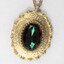 Detail of the front of a gold toned metal oval pendant with a faceted green/brown glass setting.
