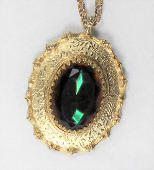 Detail of the front of a gold toned metal oval pendant with a faceted green/brown glass setting.