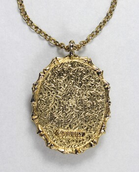 Detail of the back of the gold toned metal oval pendant and the Sarah Coventry copyright on the lower back surface.