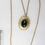 Front of a gold toned metal cable chain necklace with an oval pendant and a faceted green/brown glass setting and a black and white 5 cm scale.