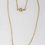 Front of a necklace with a gold toned metal chain and a small blue bird pendant and a small faux pearl. 