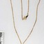 Front of a necklace with a gold toned metal chain and a small blue bird pendant and a small faux pearl, with a black and white 5 cm scale.
