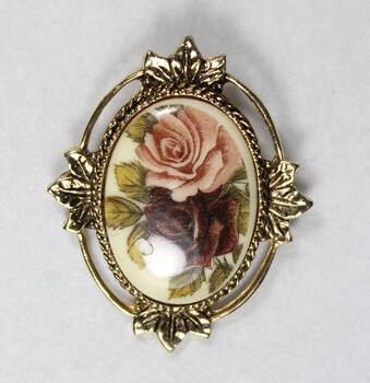 Front of a gold toned metal brooch-pendant with a cameo of one pink and one red rose.