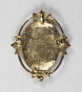 Back of a gold toned metal brooch-pendant with the Sarah Coventry copyright mark on the lower edge.