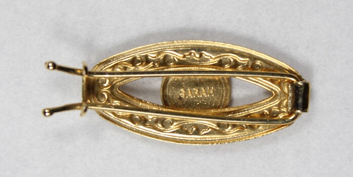 Back of a gold toned metal hair clip with a Sarah Coventry mark on the back of the circular decorative element.