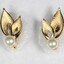 Front of two gold toned metal earrings with each earring consisting of a faux pearl and two leaf-shaped elements