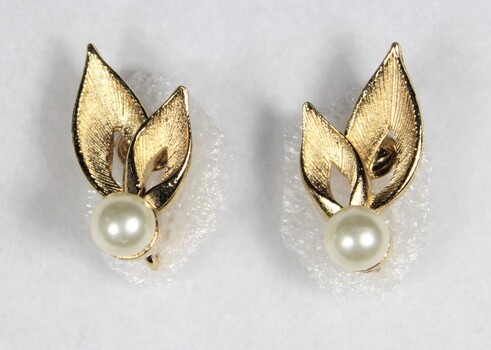 Front of two gold toned metal earrings with each earring consisting of a faux pearl and two leaf-shaped elements